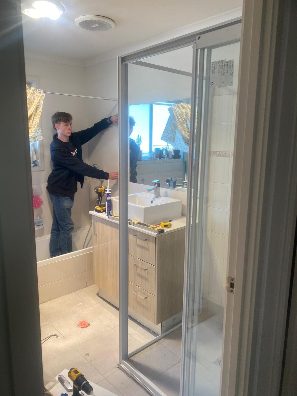 Renovation photo: worker installing bathroom mirror above vanity